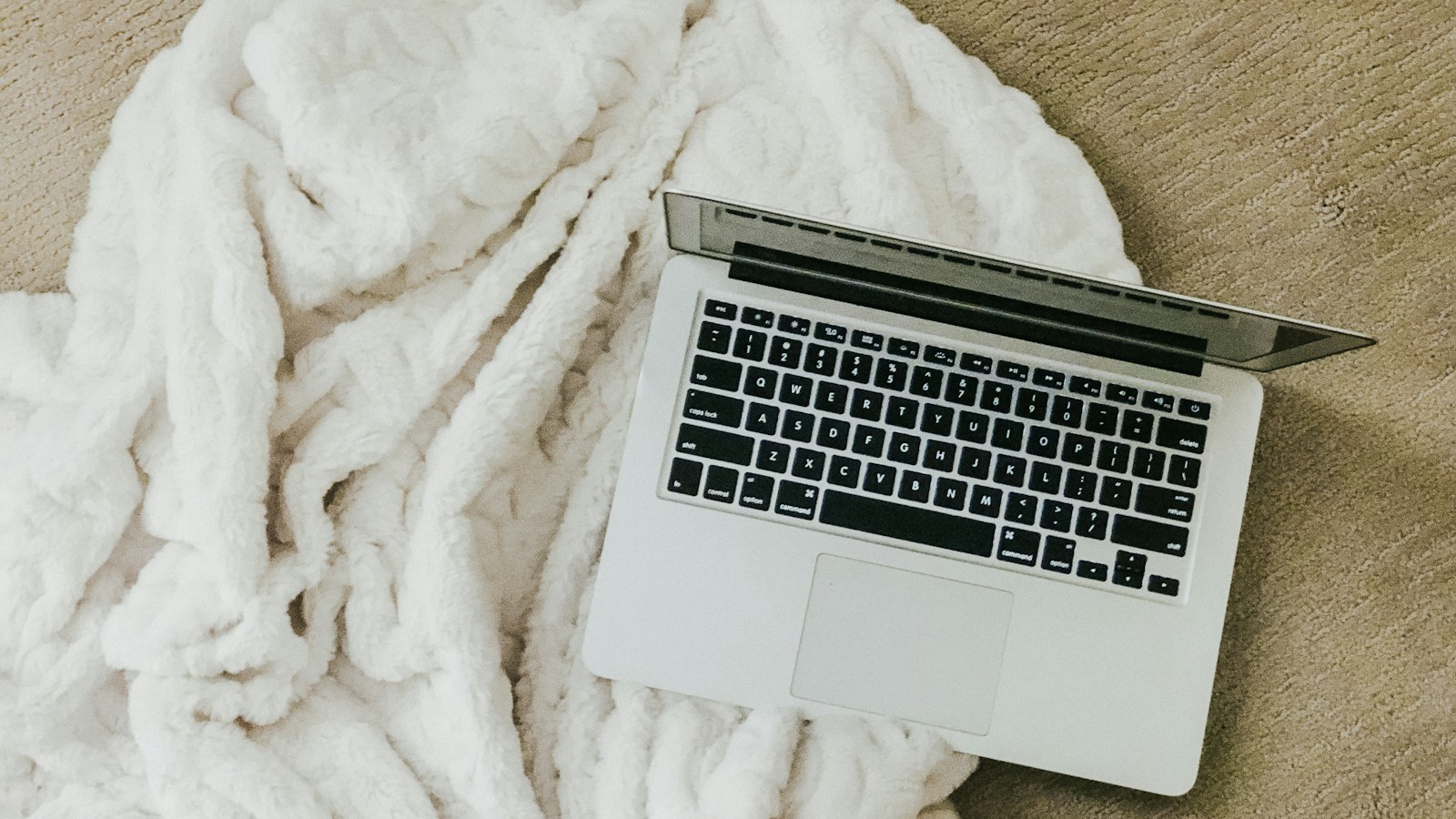 Laptop terbuka di atas selimut putih dalam suasana rumah.