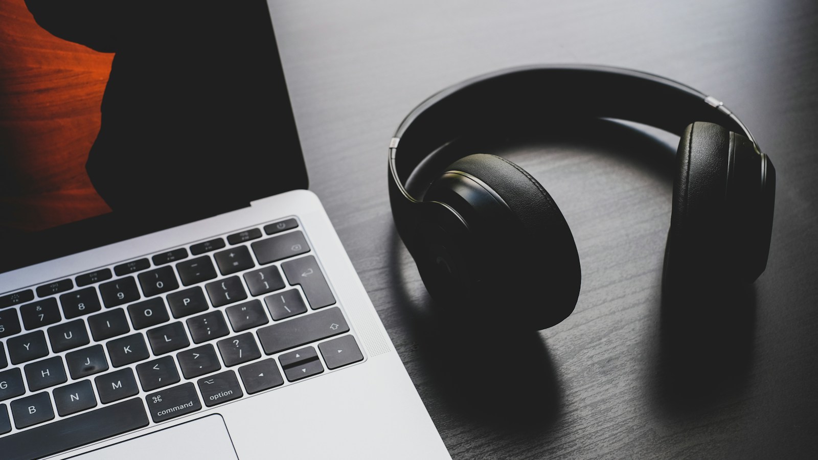 Headphone hitam di samping laptop pada meja kayu.